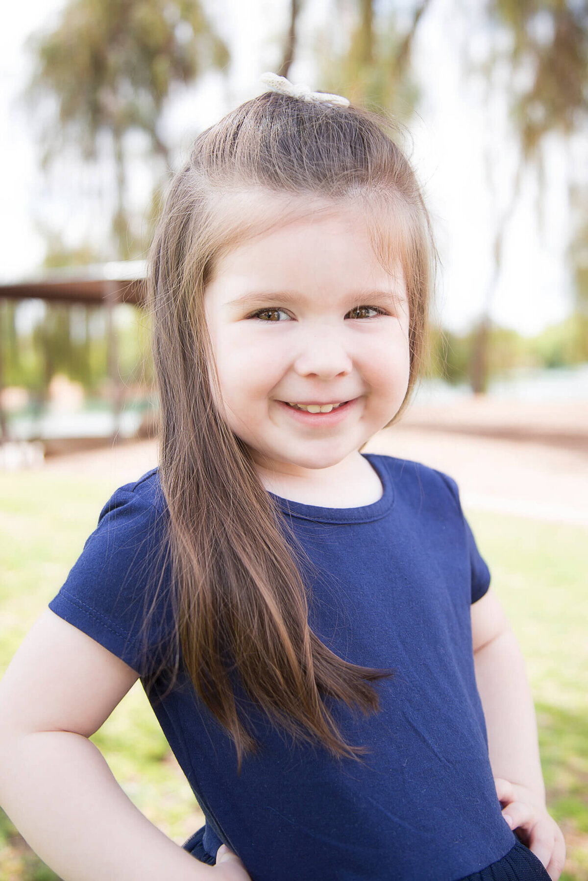 Toddler girl smiling for a portrait in a park wearing dark blue