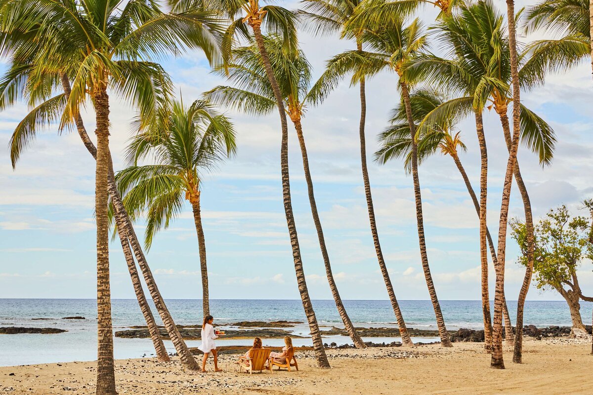 two women being served drinks on the beach among palm trees