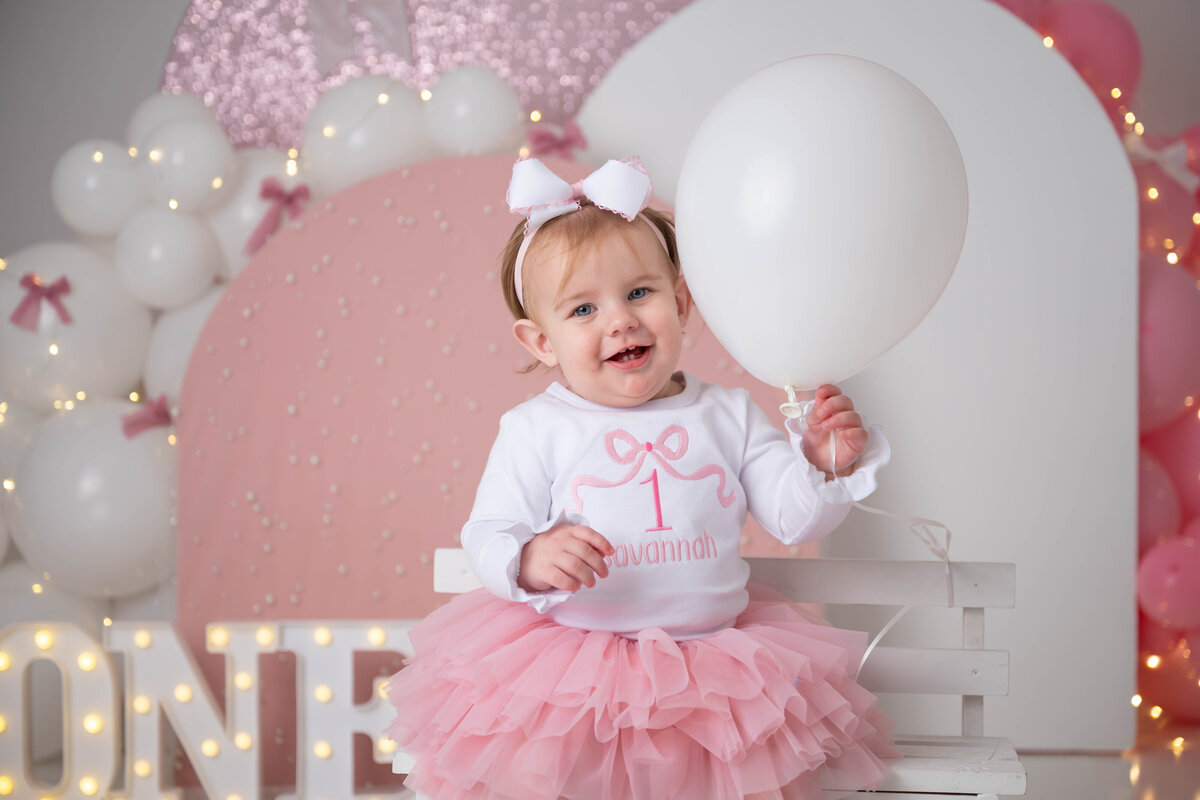 Close up of a child in a white bow shirt and pink tutu while holding a white balloon. 
