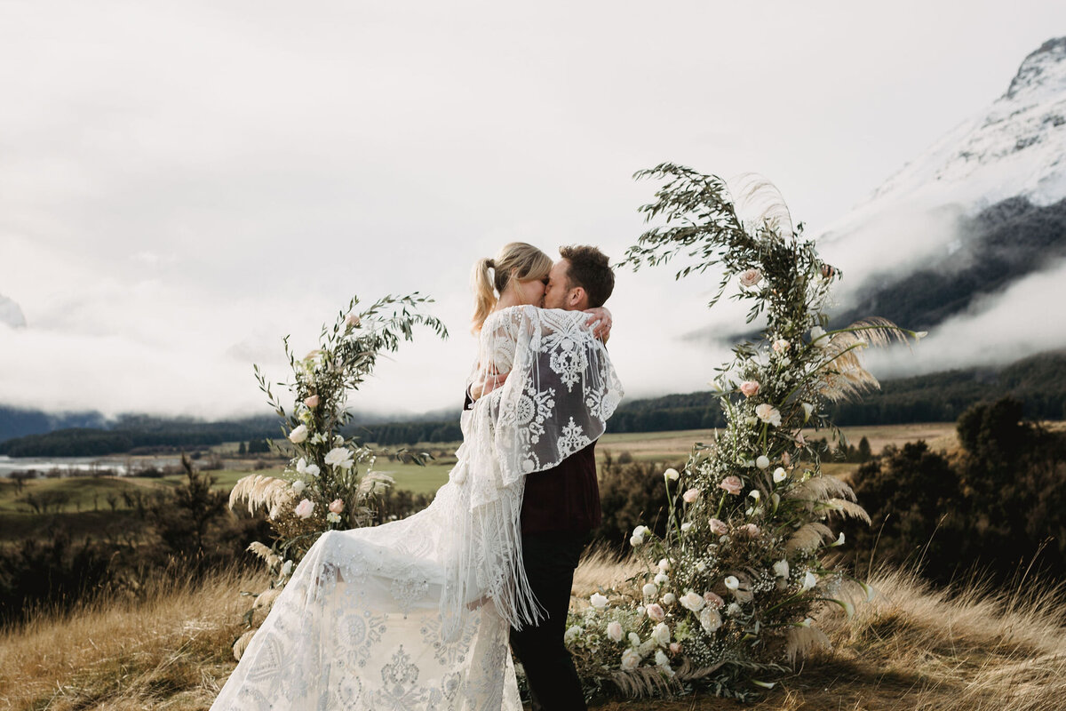 The Vase Floral Co - bride and groom kiss in Queenstown mountain scape in the middle of flowers