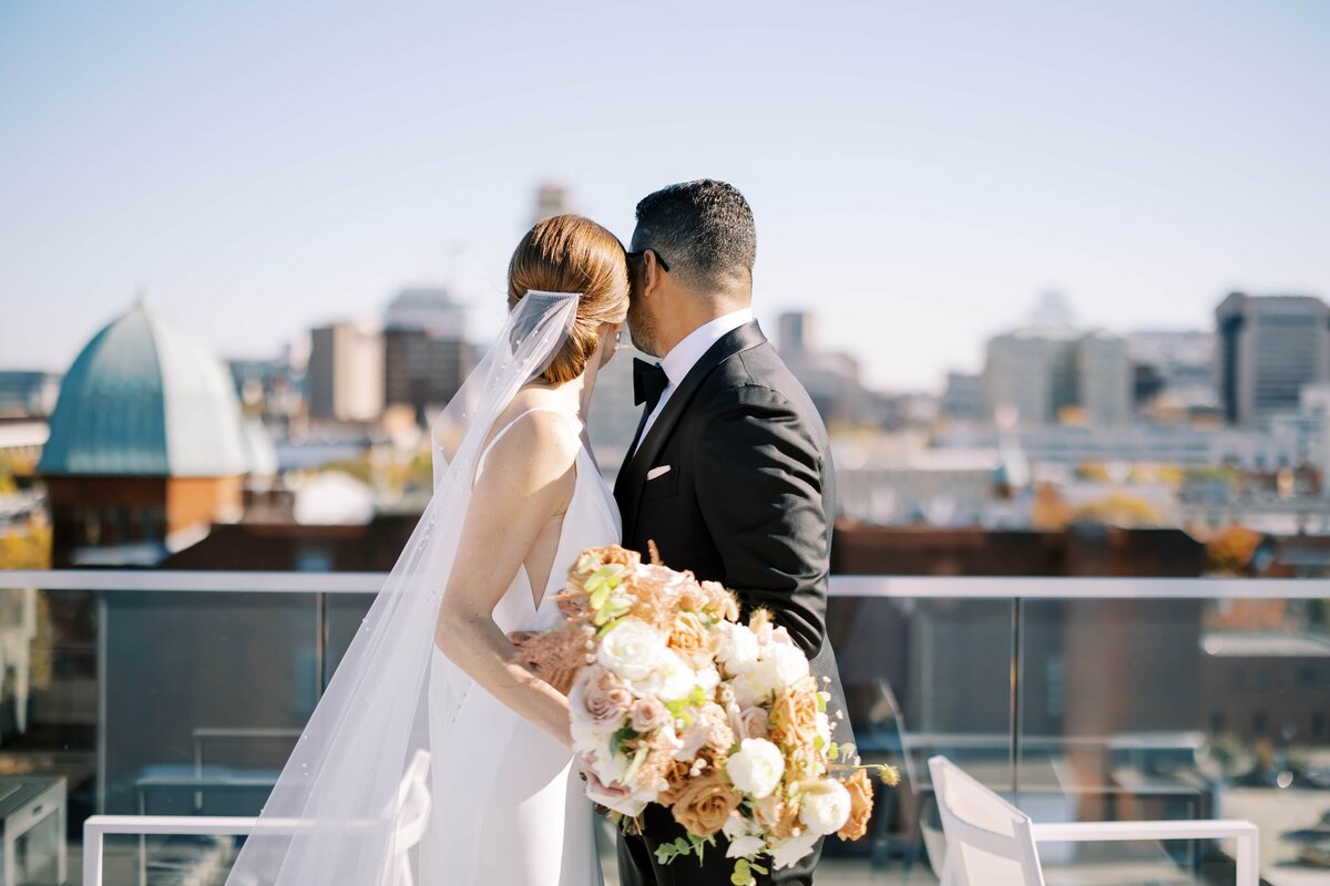 A wide view of the city of Richmond from the top of the Quirk hotel with a bride and groom standing next to each other and looking out towards the buildings