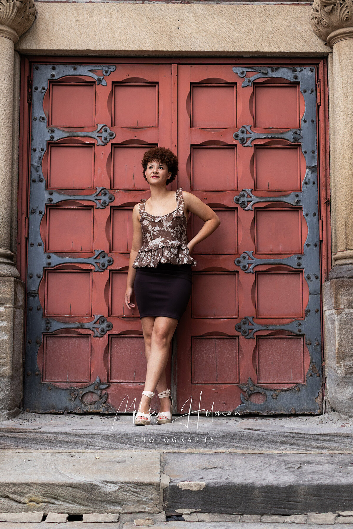 girl stands with brown skirt on next to church red doors.
