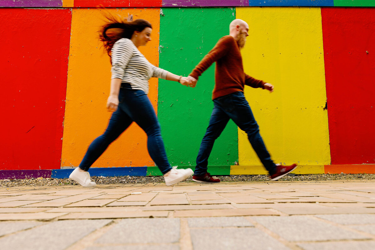 A pre wedding photo of a couple running down a street in Manchester with a multi colour backdrop