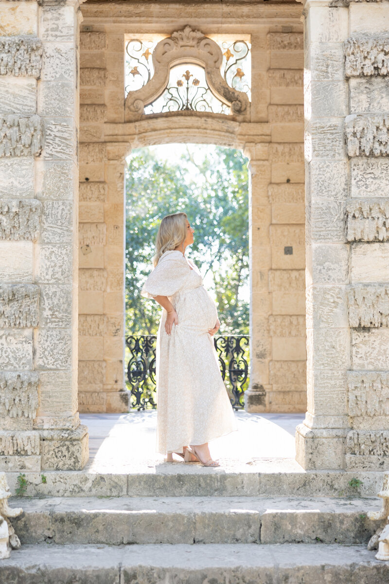  A mother-to-be glows in a golden light as she stands in an arched stone doorway.
