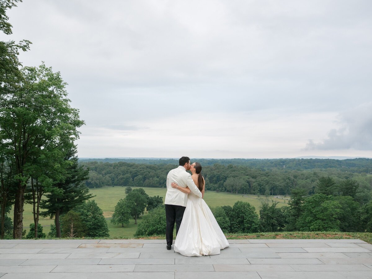 Kara and Nick sharing a kiss on the terrace with the valley spread out behind them