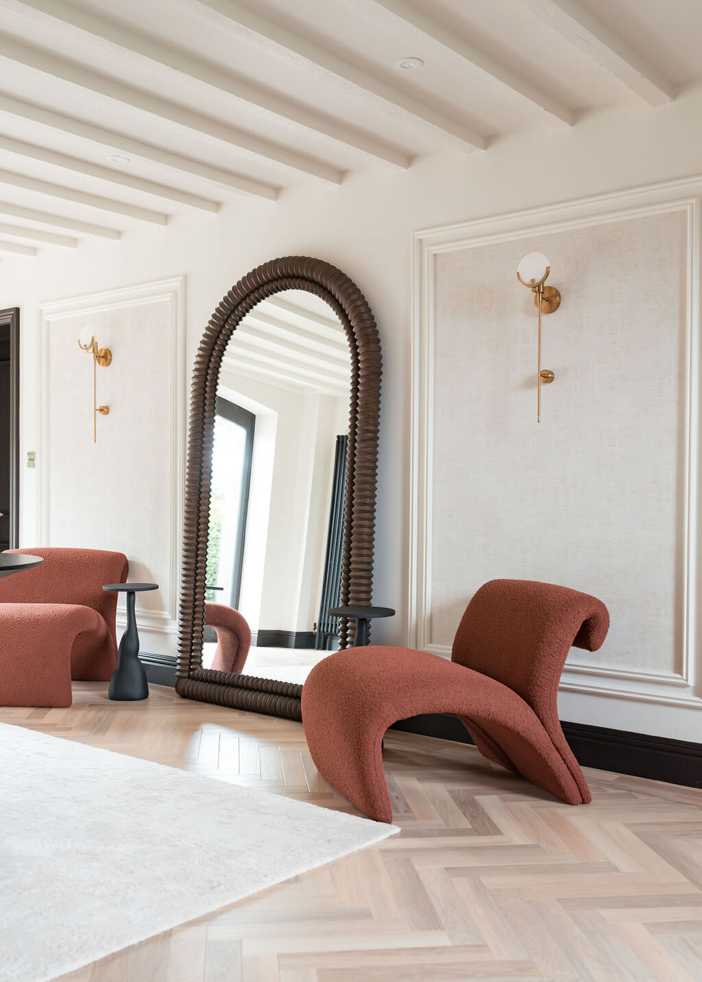 A modern foyer features two red chairs, with a large mirror between them. The flooring is light and the walls are white.