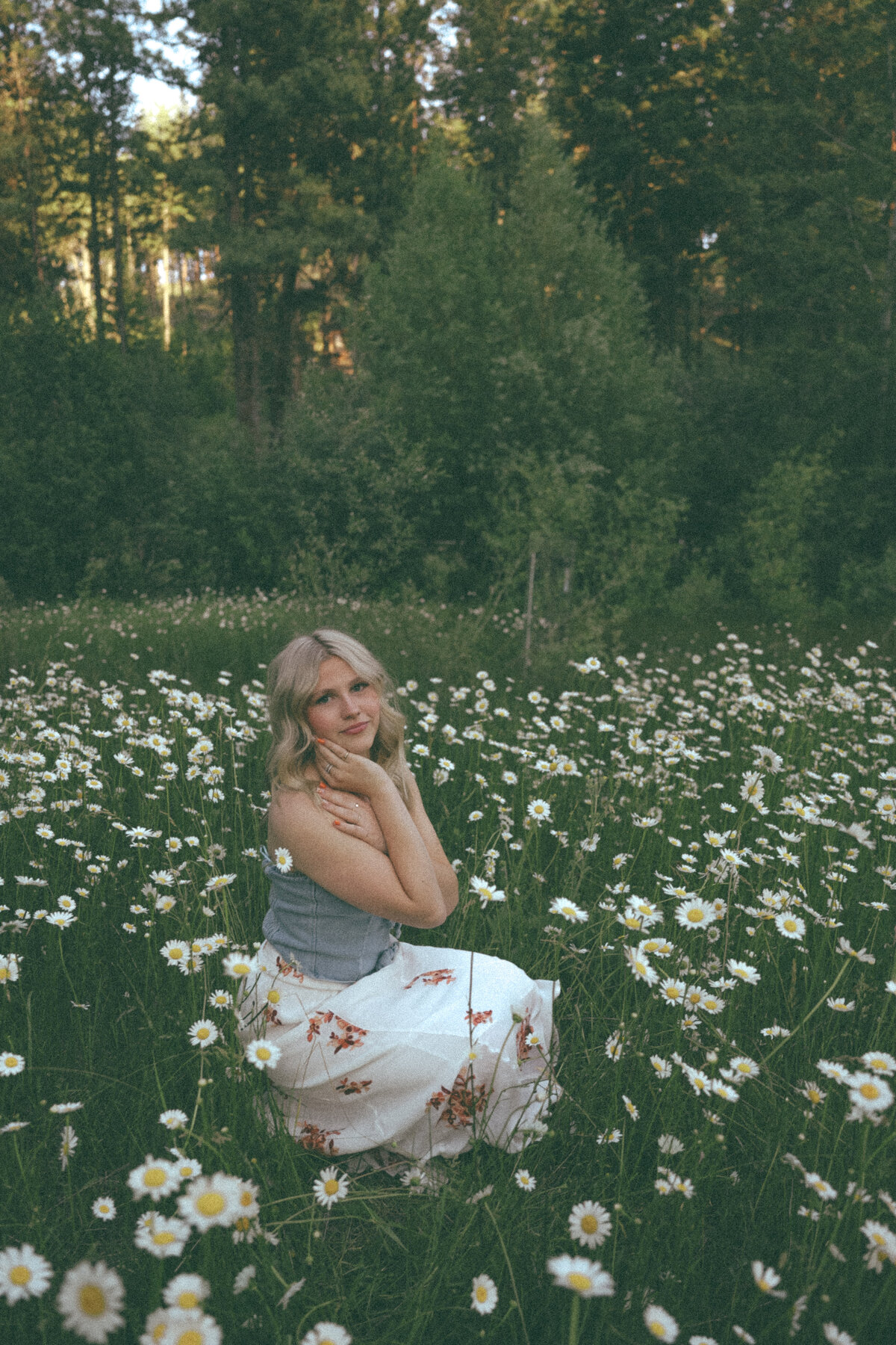 Natural Senior Portrait of Girl in Navy Dress Sitting in Field with Wild Grasses and Soft Light