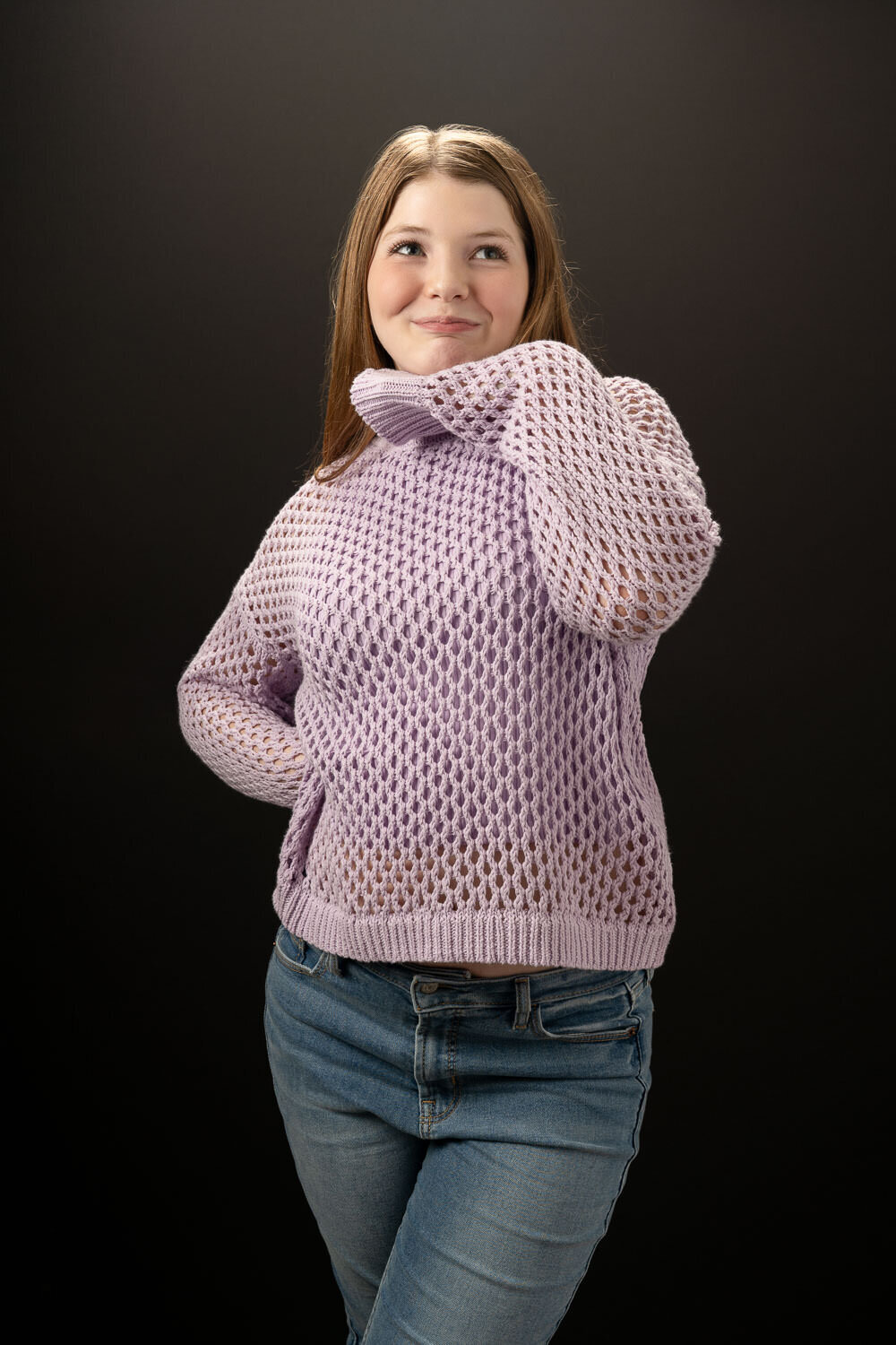 Candid studio portrait of a teenage girl wearing an oversized sweater, striking a playful and cute pose.