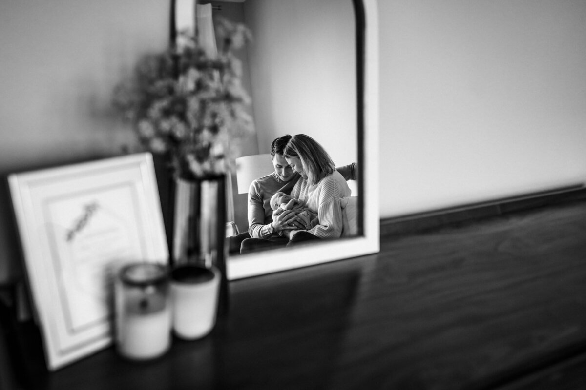 reflection in mirror on dresser of mom and dad sitting in bed with newborn