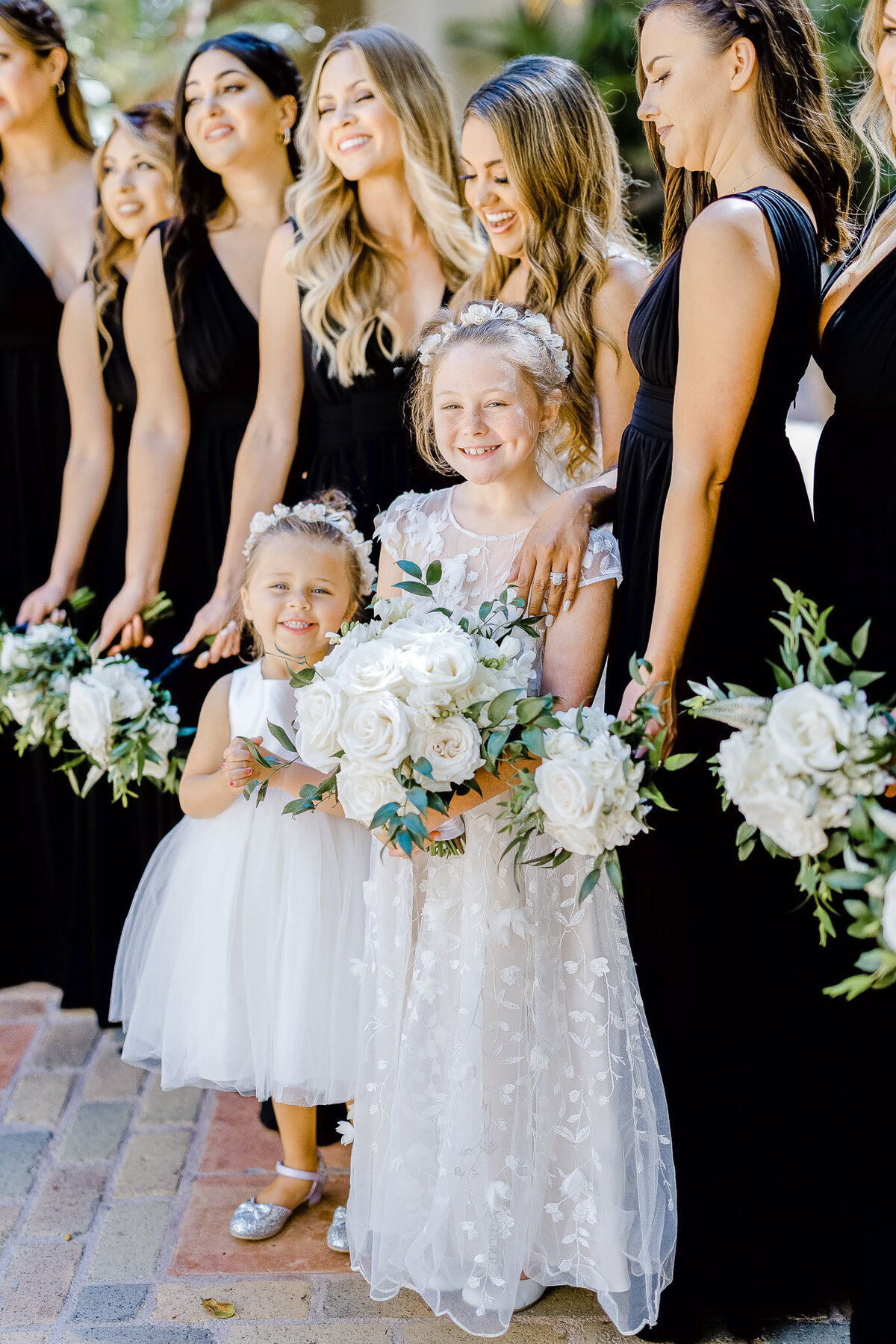 Two flower girls in white dresses smile brightly while holding bouquets, surrounded by the bridal party at the Ritz-Carlton Laguna Niguel