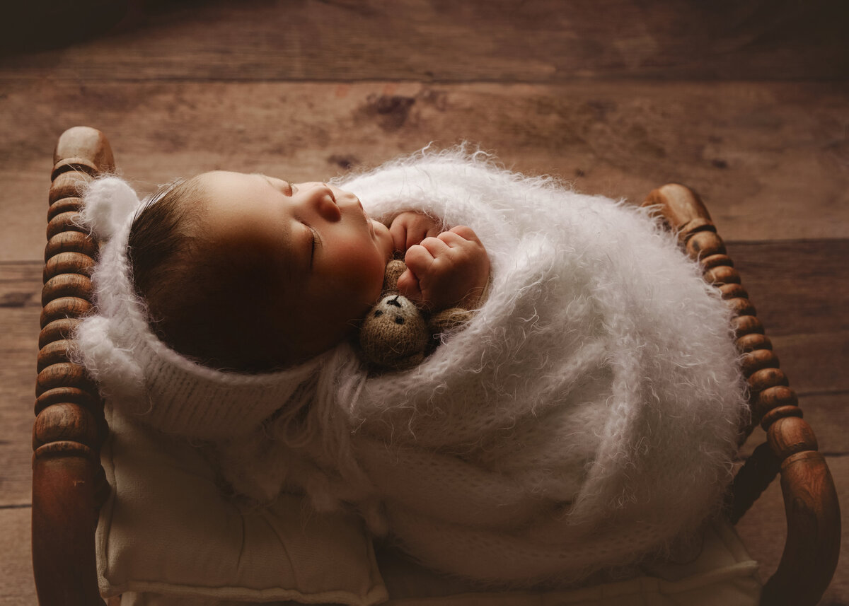 baby boy holding teddy besr laying in bed wrapped up near bellevue
