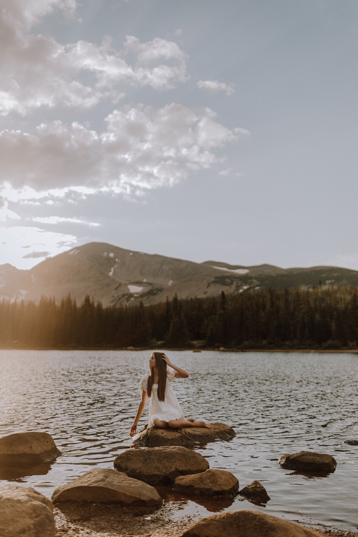 senior girl in golden light posing on rock in middle of lake