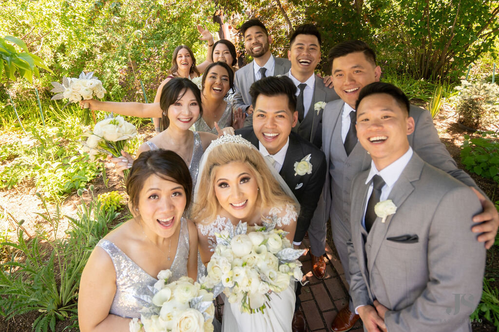 Bridal party with groomsmen in grey suits and the bridesmaids in silver dresses pose with the bride and groom with white bouquets.