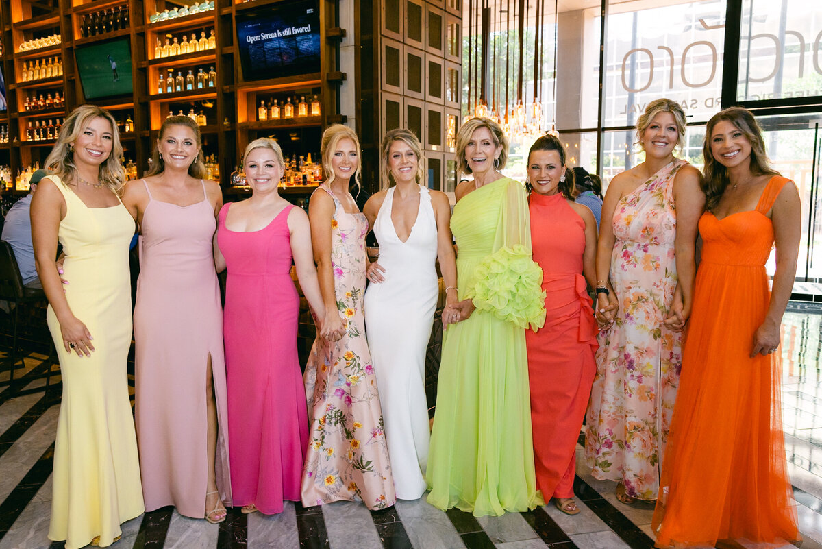 A wedding photo of a bride in her white dress with her bridesmiads who are wearing different colored bright dresses