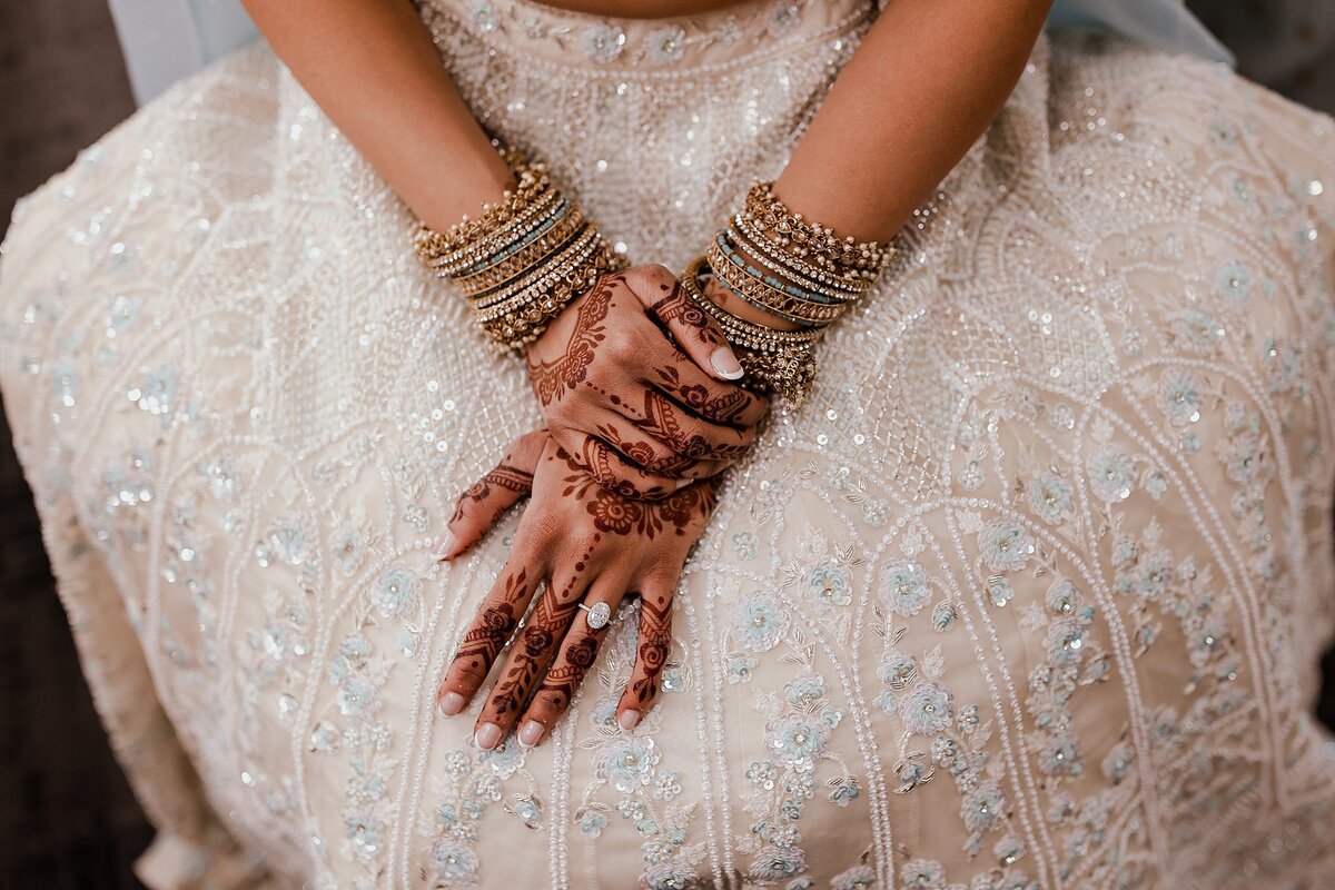 Indian bride wearing a white beaded saree shows off her white and gold wedding bangles and her  mendhi wedding henna.
