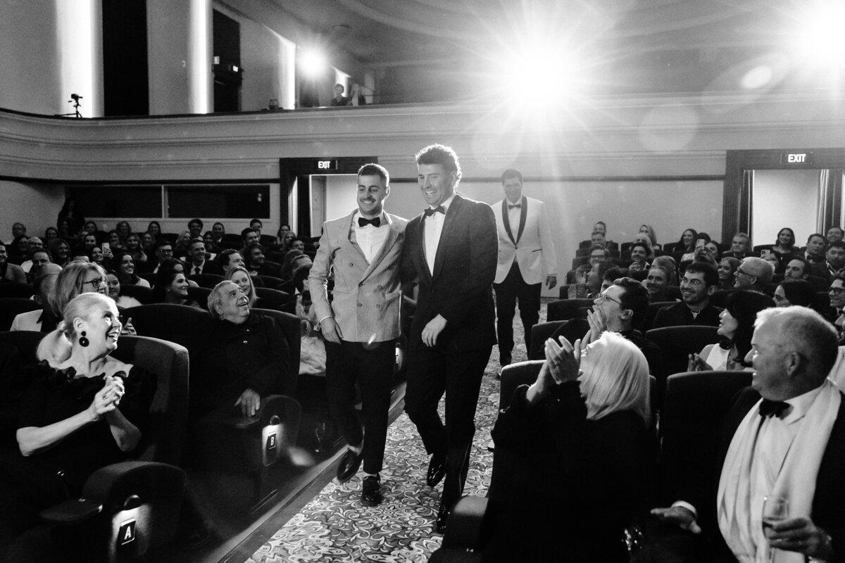 The newlyweds walk on the aisle of the theatre as guests cheer them on.