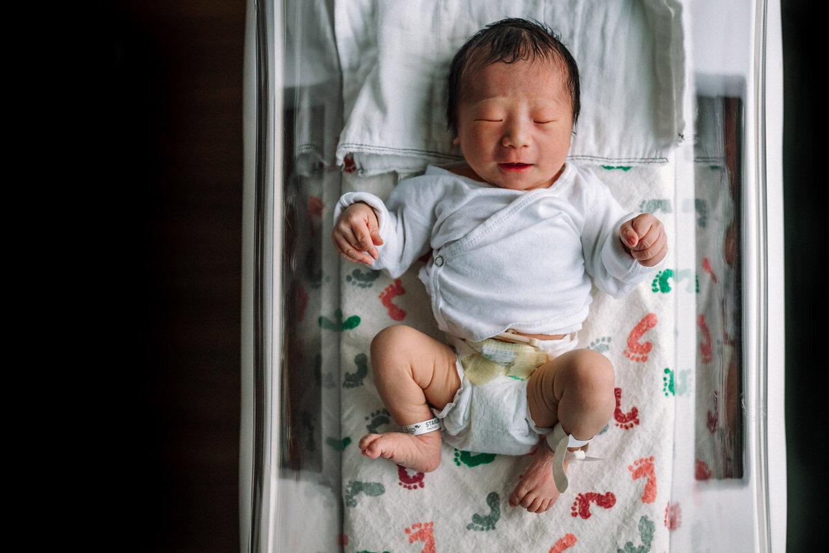newborn paying in hospital bassinet next to window