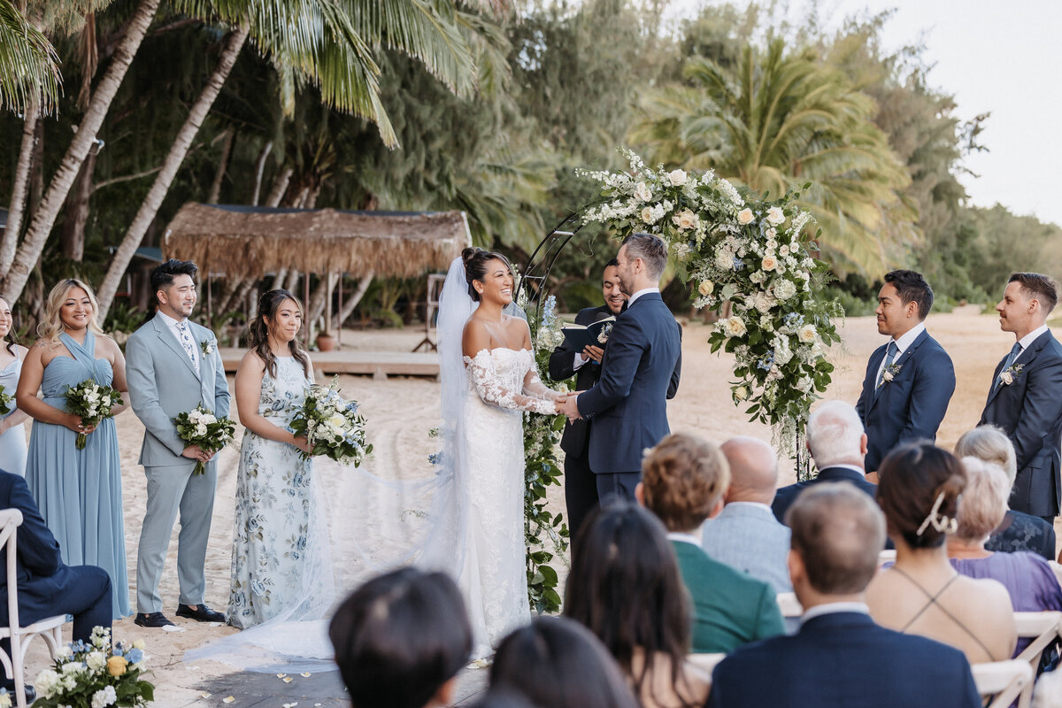 Bride and groom ceremony at Kualoa Ranch on the beach, holding hands with palm trees and ocean in the background
