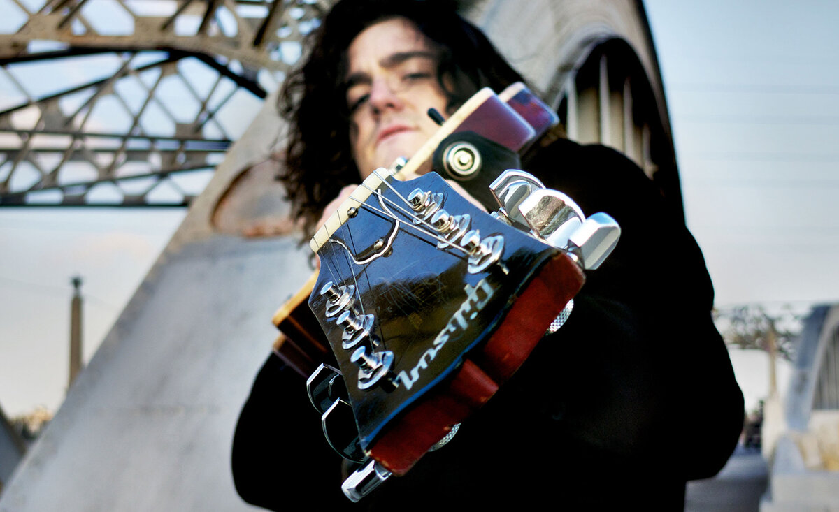 Male musician photo Robert Fortune close up wearing black suit pointing electric guitar forward