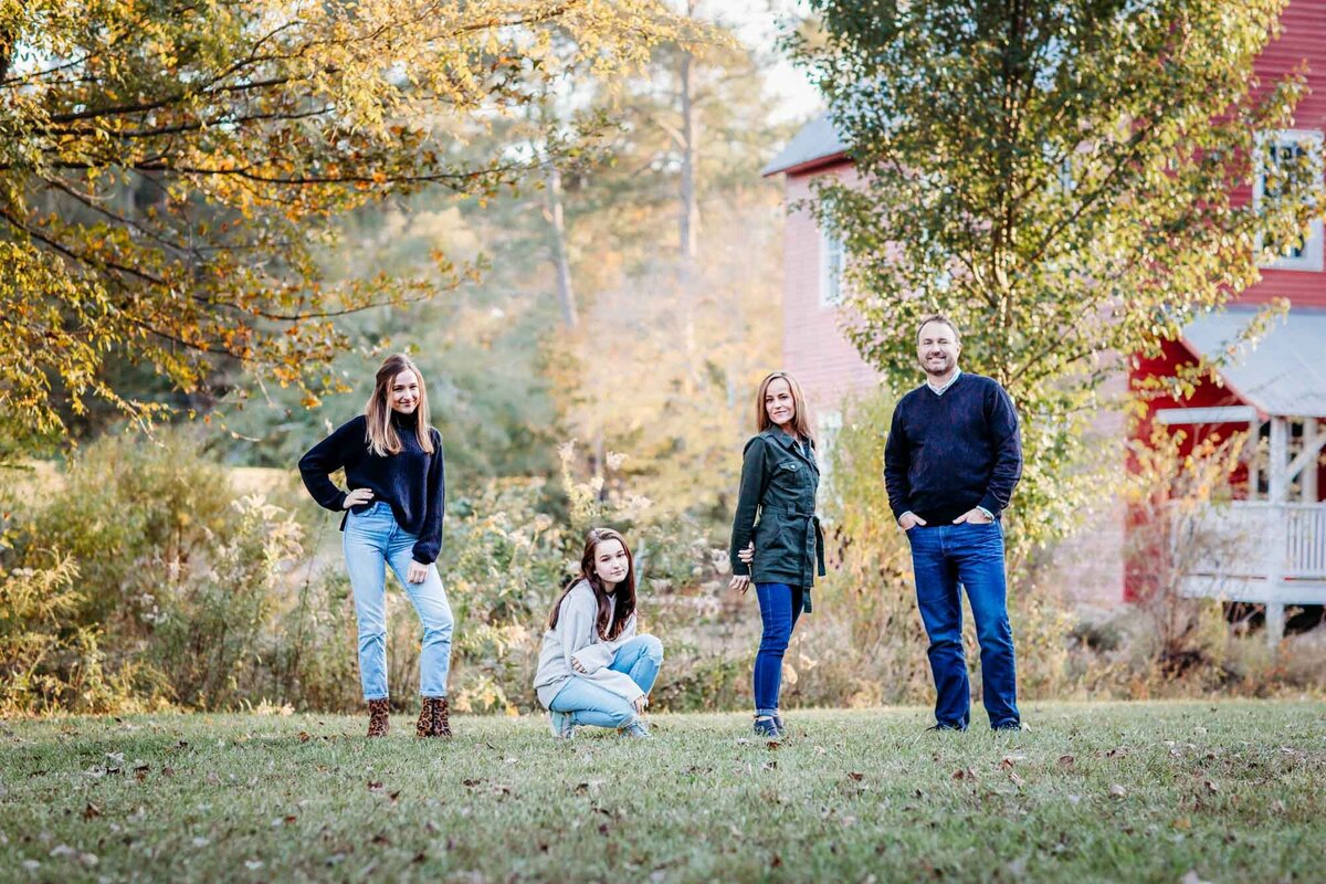 A powerful family portrait of four people all in a different stance and looking seriously into the camera at Starrs Mill with fall leaves and a red barn behind them.