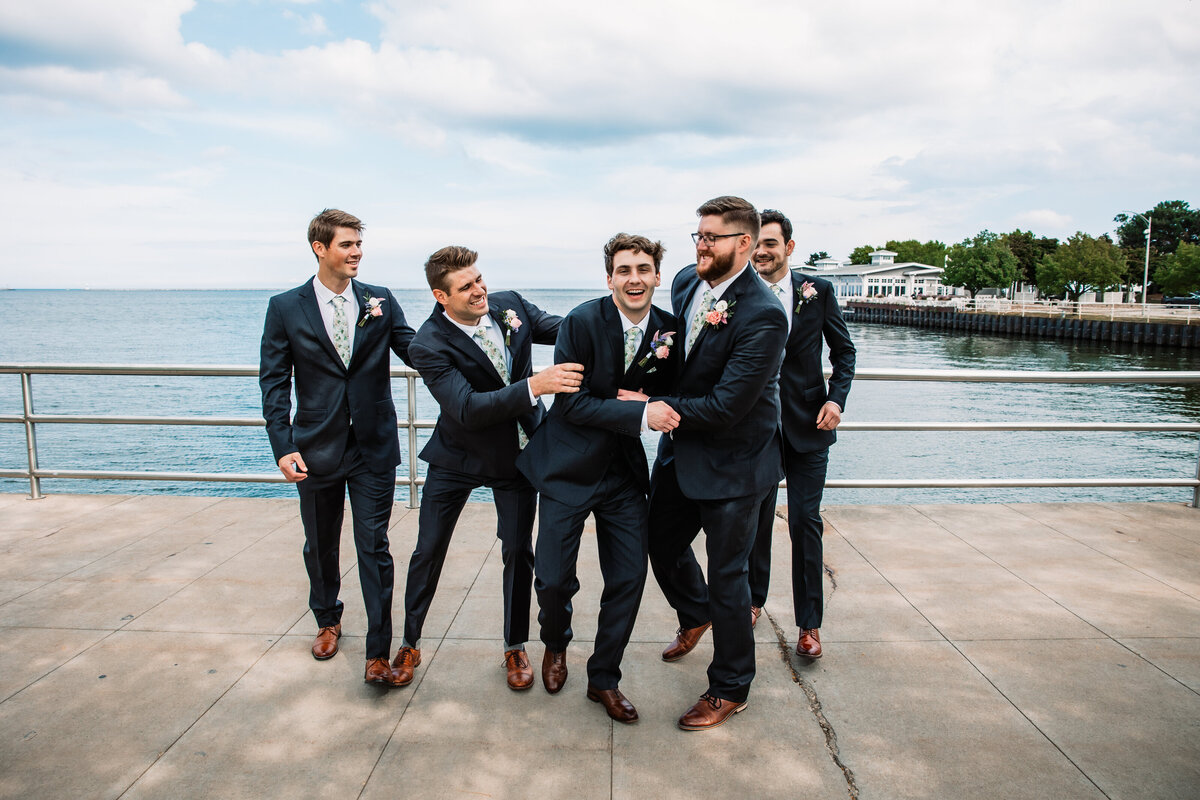 A groom is pushed around by his groomsmen by the water