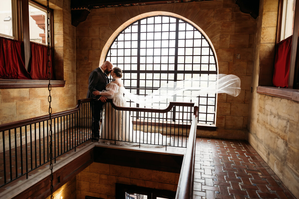 bride and groom kiss while veil floats in the air in front of the balcony window at treasury on the plaza