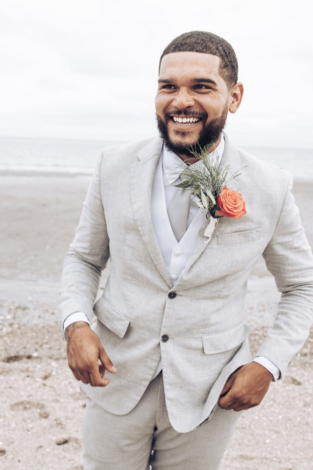 groom laughing while standing on the beach