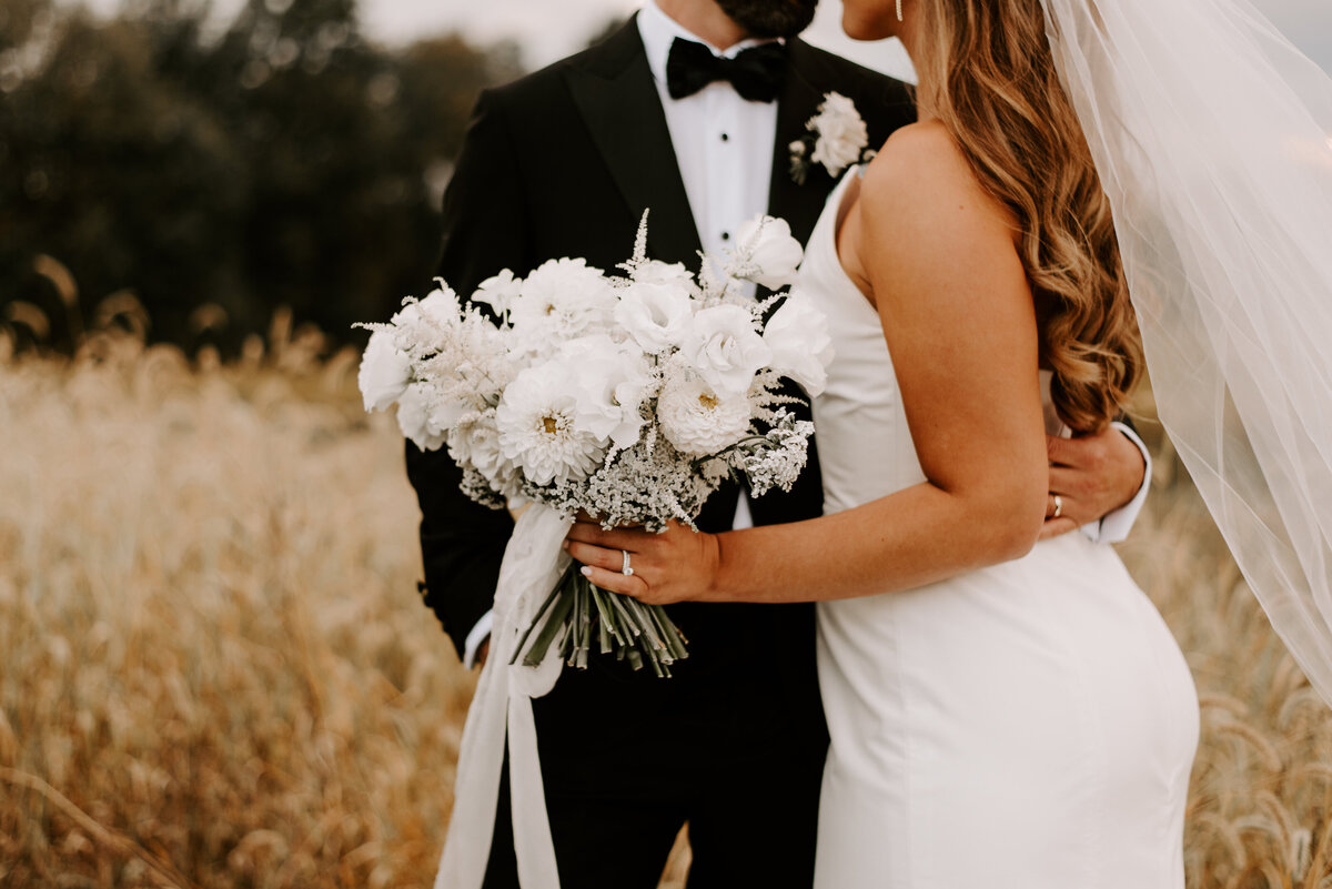 Close-up of a white bridal bouquet as the bride and groom embrace.