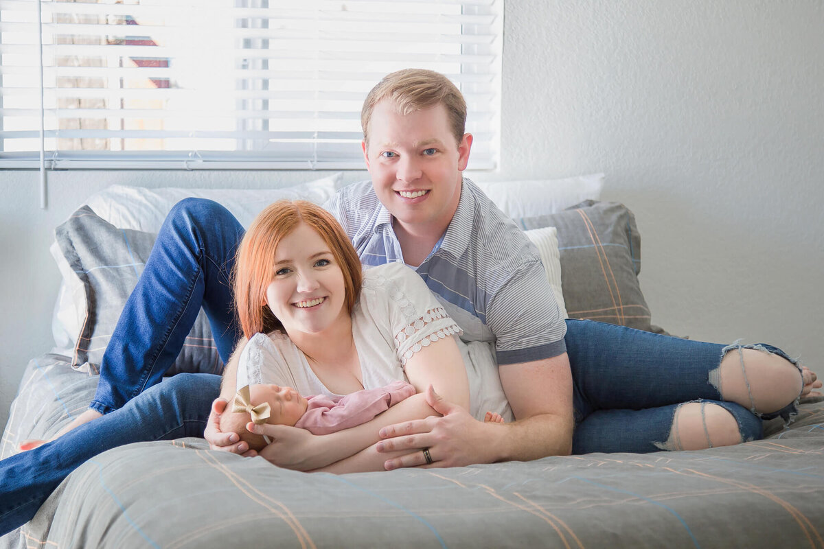 Couple smiling snuggle don bed with newborn baby girl capturing  newborn moments