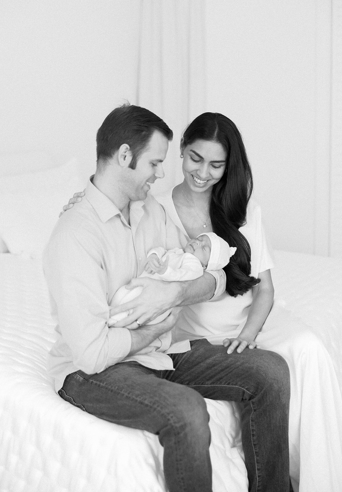 A loving couple gazes at their newborn while seated together in their home during a Florida Keys portrait session.
