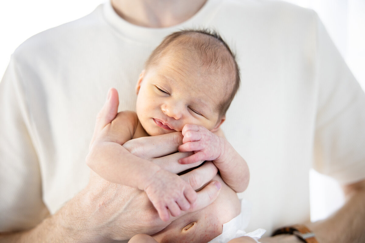 Newborn infant in dad's hands in a light filled room