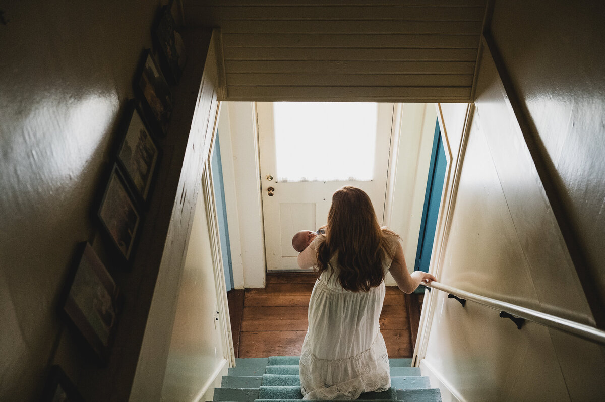 Mother holding newborn on stairs during an in-home Connecticut photography session