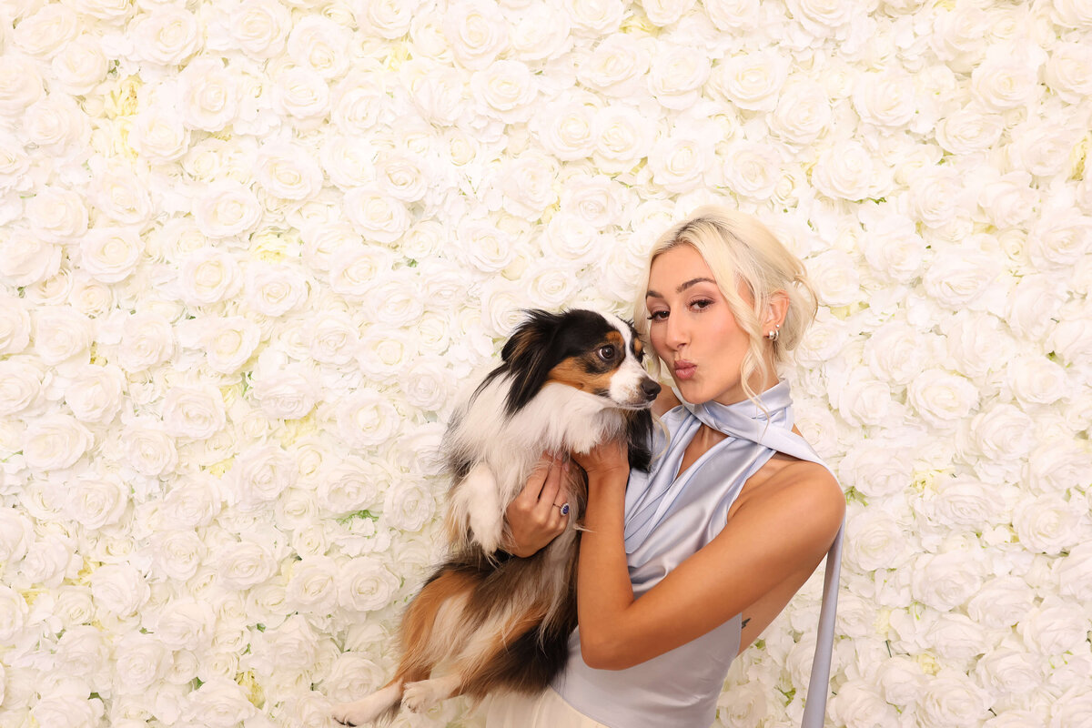 A woman and her dog in front of a wall of white roses, representing the backdrops available when ordering this Eugene photo booth rental for weddings and events.