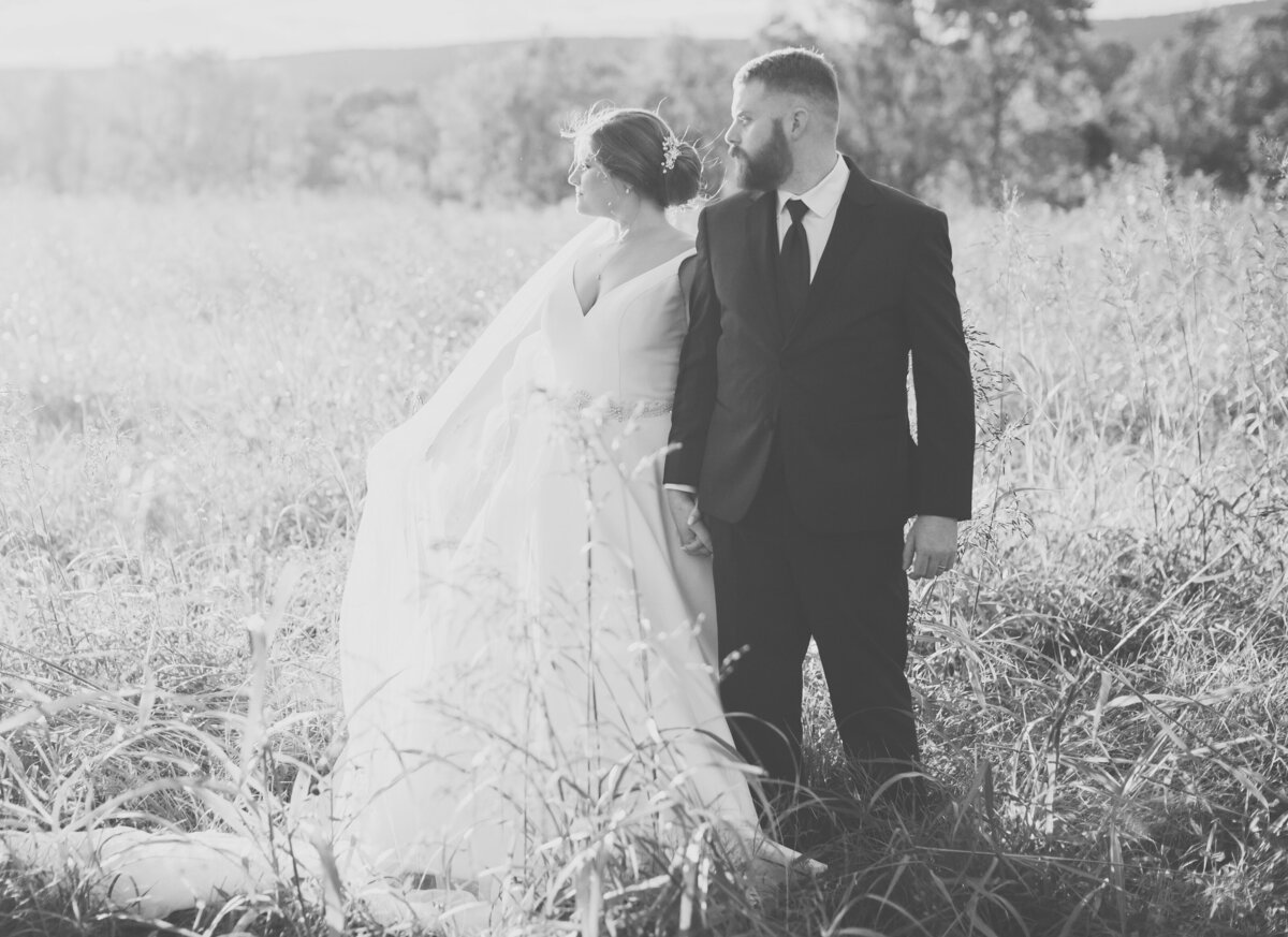 Couple walking through tall grass in black and white photo during Eastern North Carolina wedding portraits.