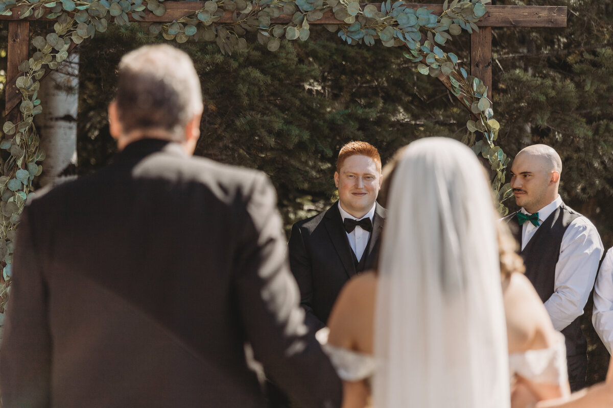 Groom looking at his bride as she walks down the aisle during wedding ceremony 