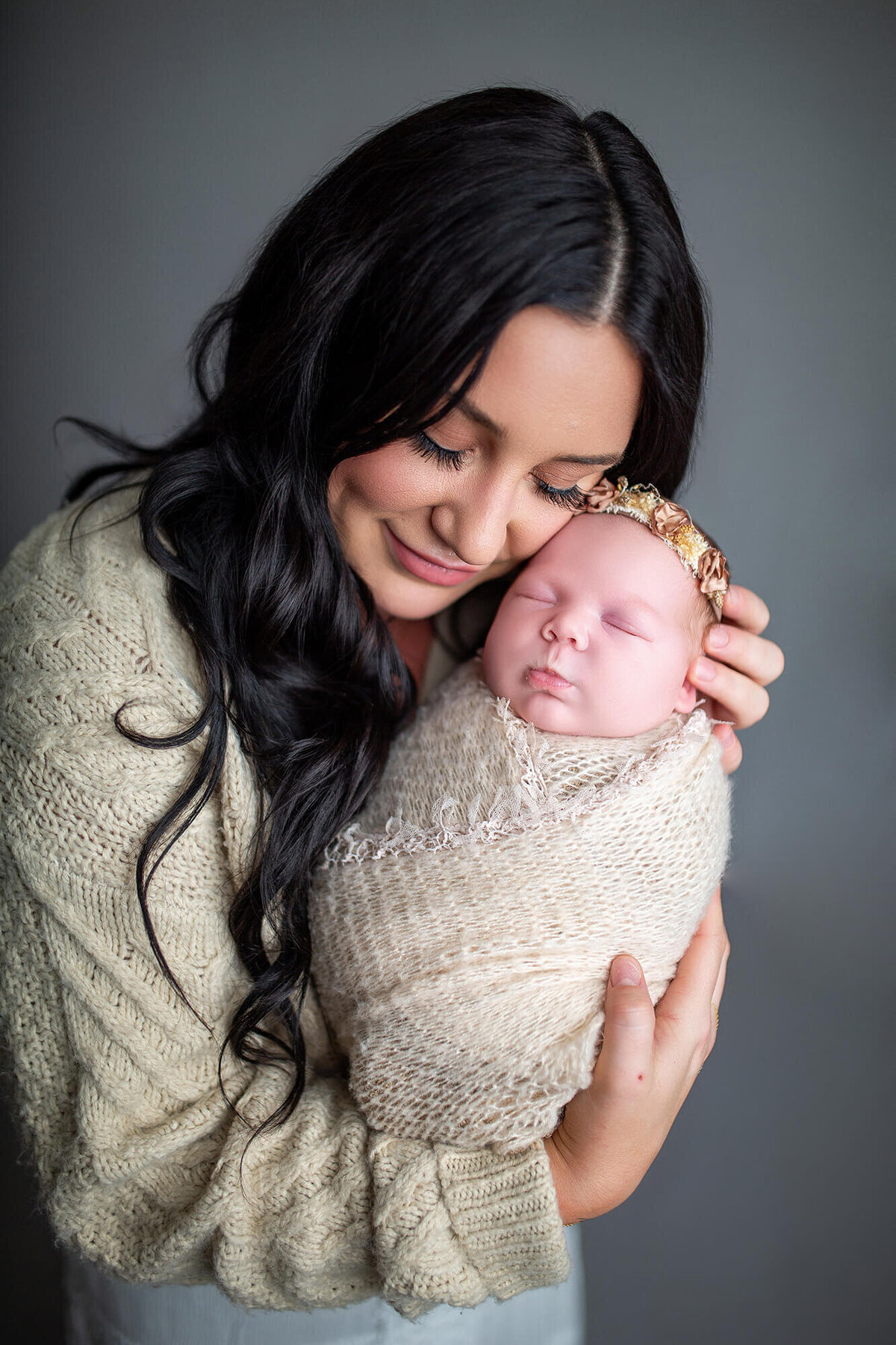 Mother snuggling cheek to cheek with newborn sleeping baby in a flower crown 