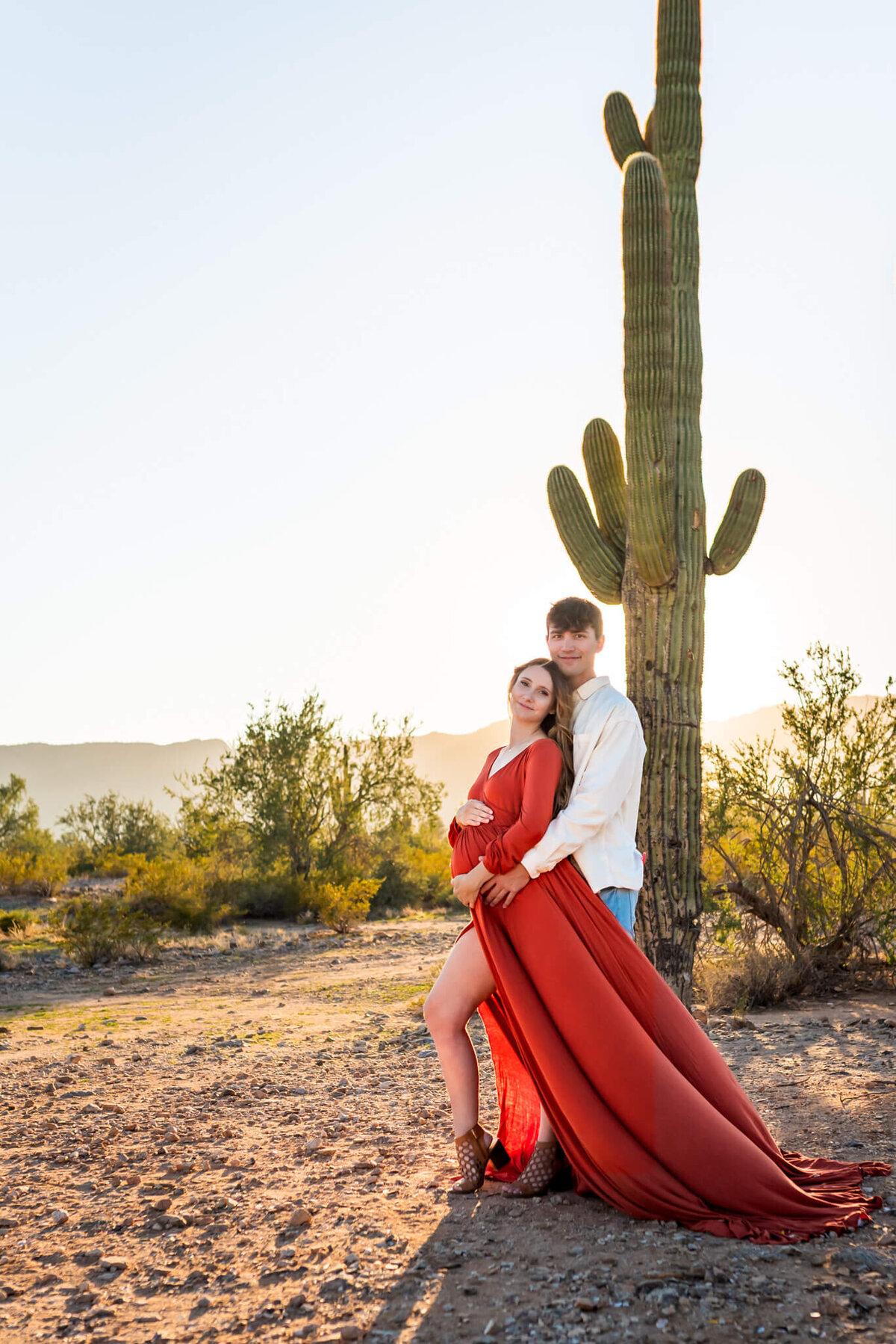 portrait of expecting mom leaning against her husband near saguaro at sunset. Taken by Cactus & Pine Photography