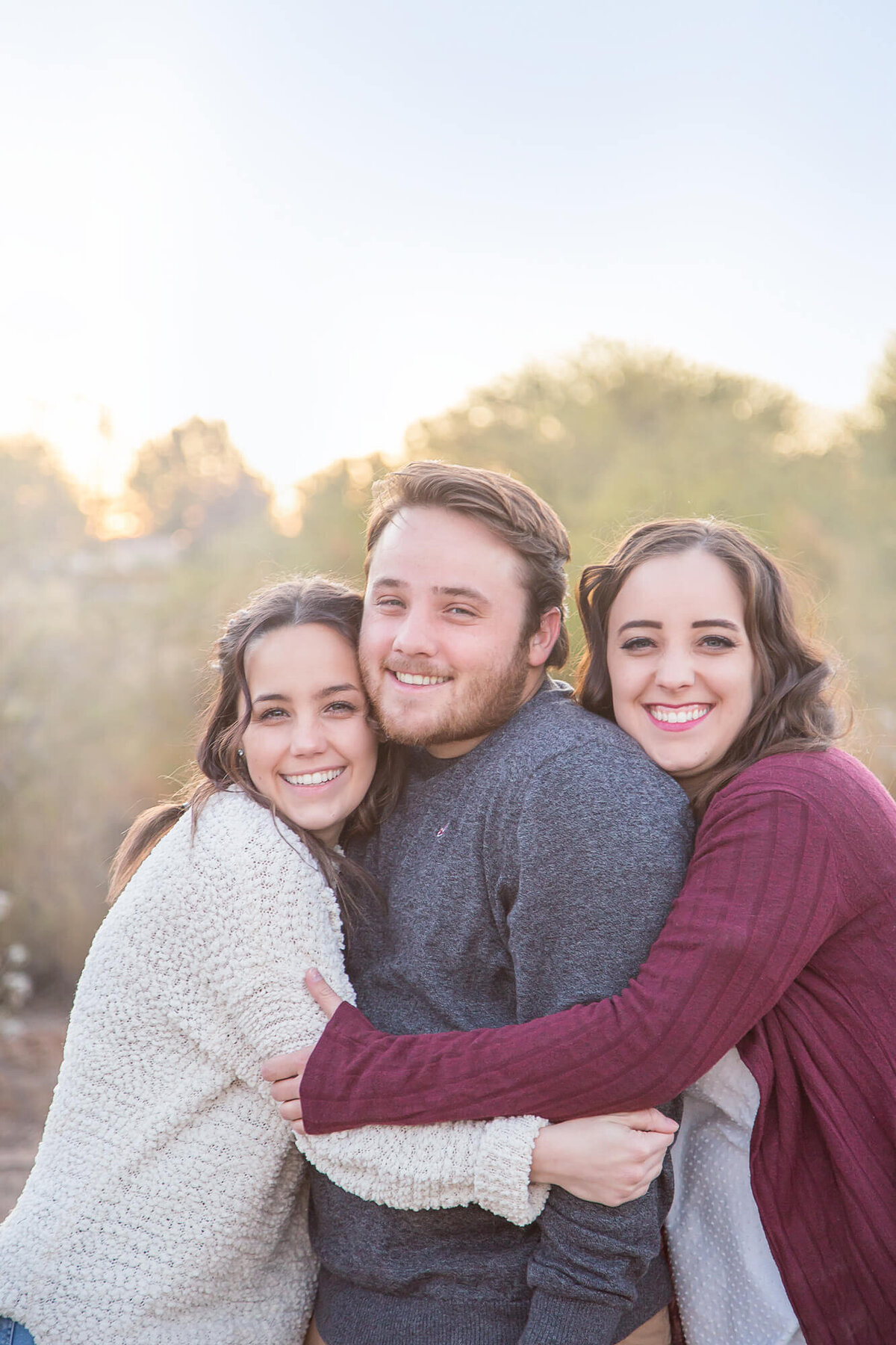 handsome brown haired man hugged by sisters in maroon and white shirts