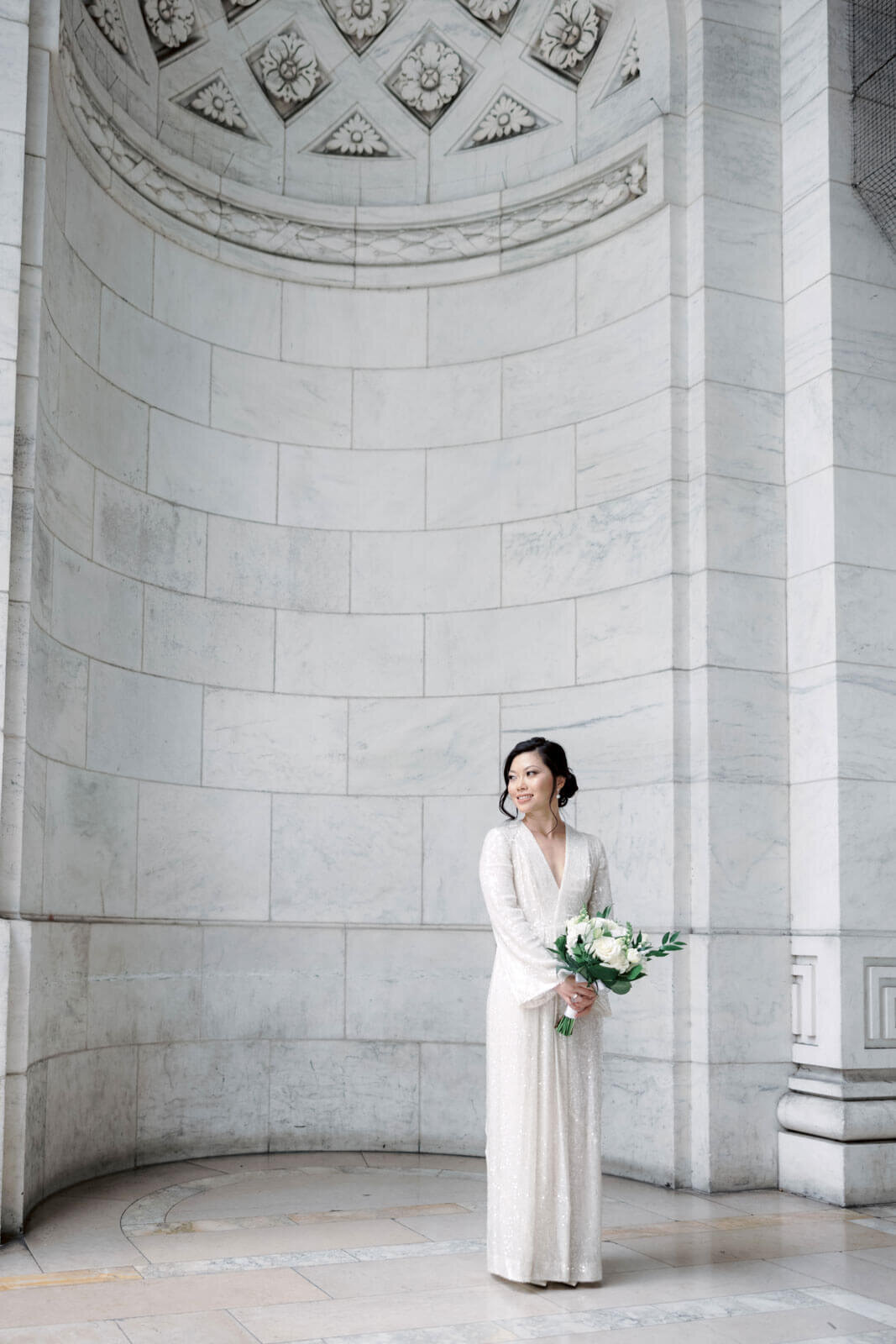 The bride is holding her flower bouquet inside the New York Public Library, NYC, with very high ceiling. Image by Jenny Fu Studio