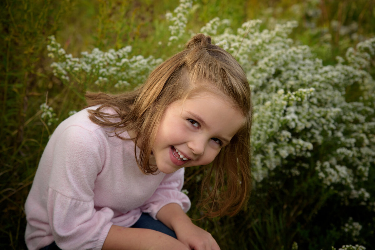 Portrait of a young girl sitting and giggling in a long grassy field at Fonferek Glen County Park near Green Bay, Wisconsin.