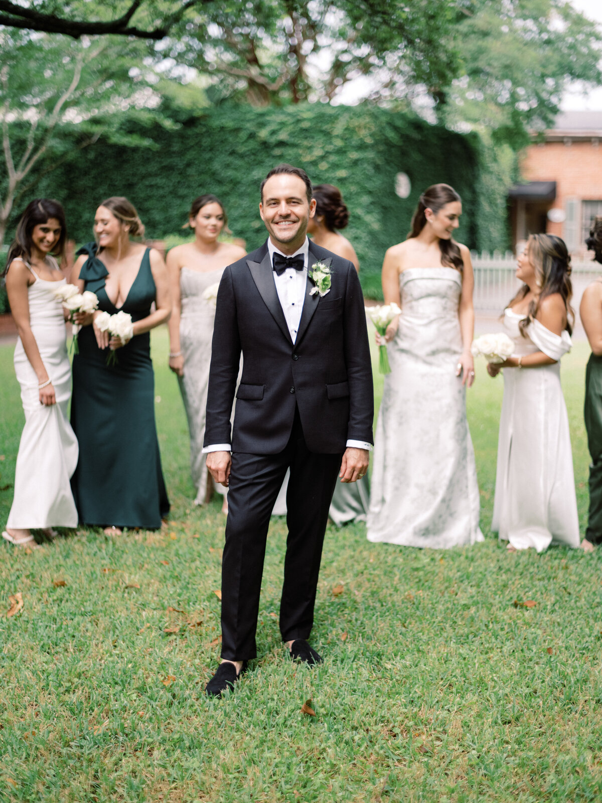 A confident groom poses elegantly in his formal suit while surrounded by bridesmaids, capturing the essence of joy, elegance, and celebration in a beautiful setting.