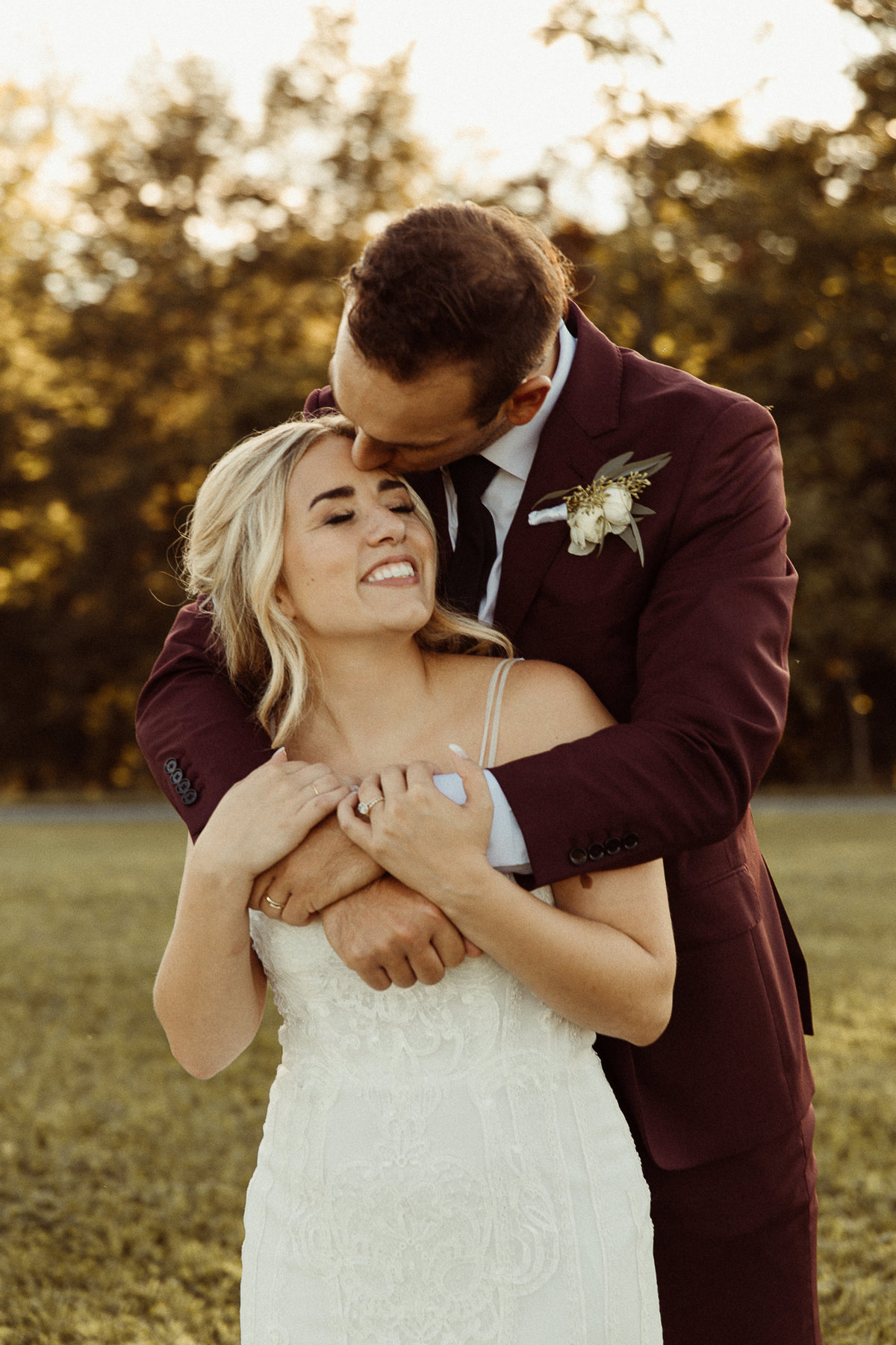 groom in maroon suit, kissing and wrapping arms around bride at hayloft on the arch