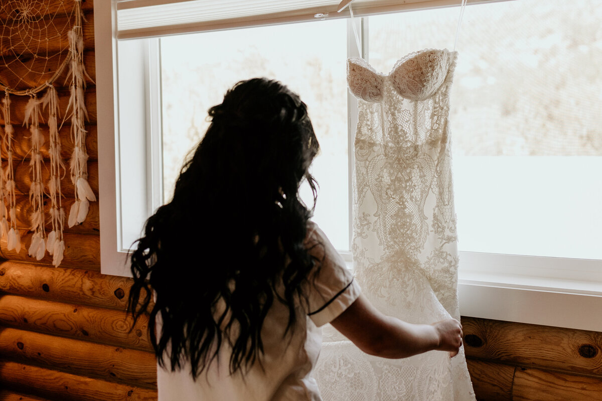 bride looking at her wedding dress hanging in a window