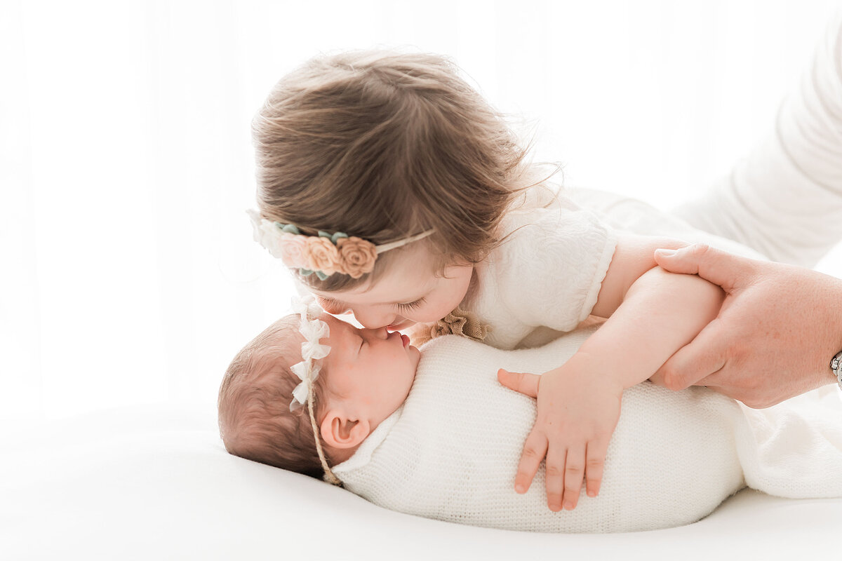 a little girl kissing her newborn sister