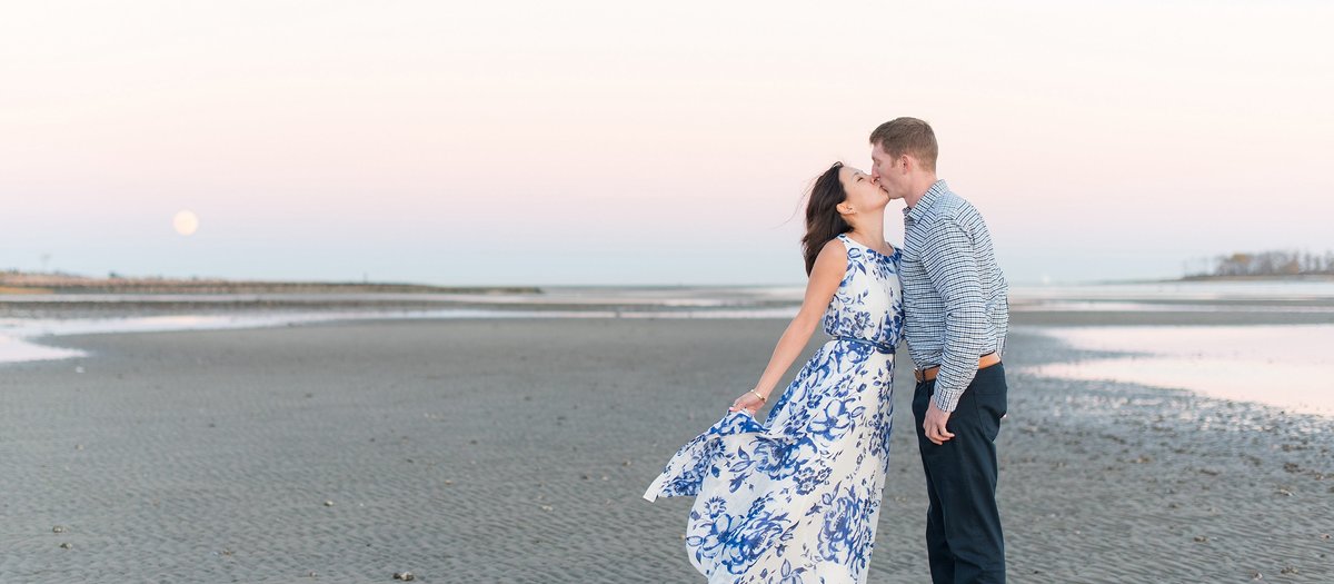Couple kisses with their reflection in the water and a pink sky at a engagement session at Silver Sands State Park in Milford, Connecticut Photo