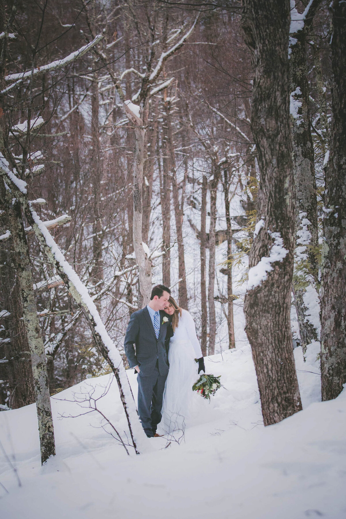 Bride and groom are surrounded in snowy landscape.