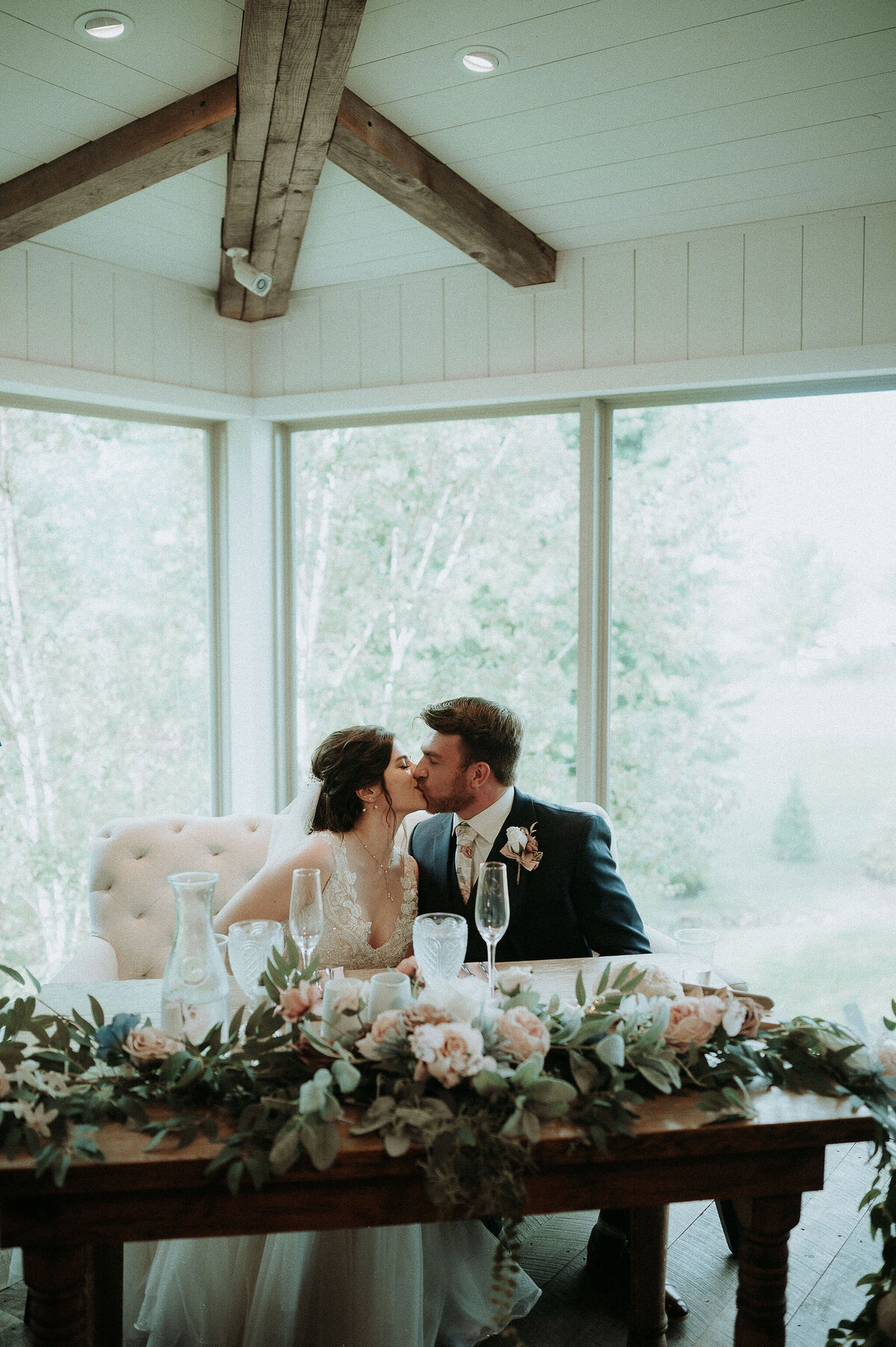 a bride and groom kissing at a sweetheart table covered with blush roses and greenery at the Willowbrook wedding venue