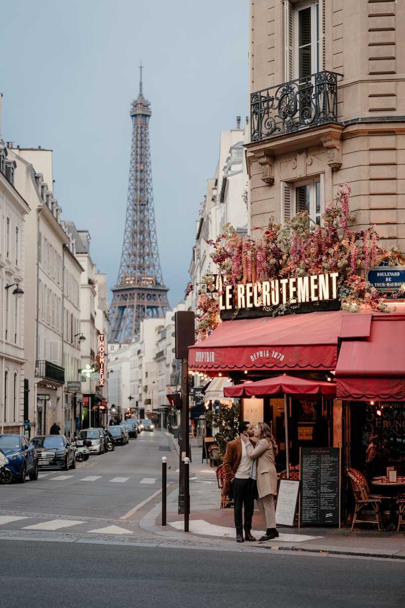 Séance photo de couple à Paris devant la brasserie Le Recrutement, avec la tour Eiffel en arrière-plan, capturant un instant romantique et élégant.