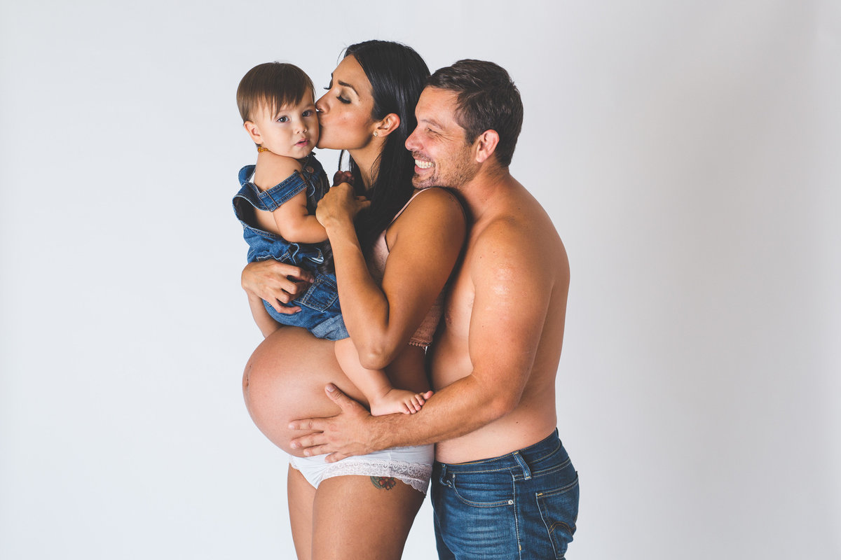 Family maternity session, pregnant mother holding toddler, dad holding mother's belly in photography studio in San Antonio.