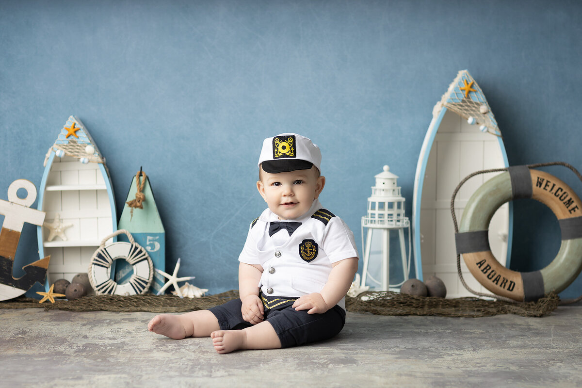 Baby boy dressed as a captain for a nautical-themed session with decorative boats, anchors, and starfish, captured by a Dallas milestone photographer.